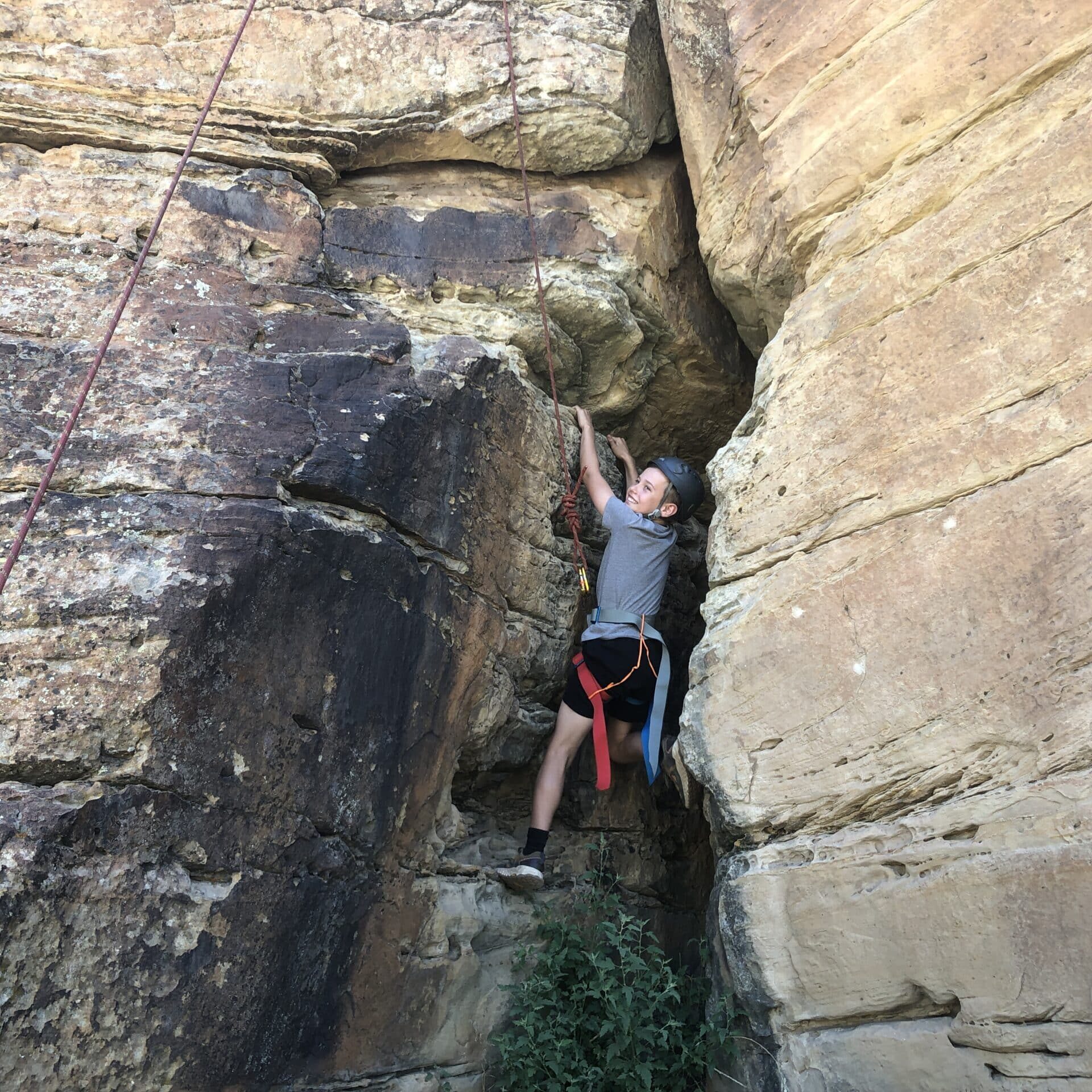 a young boy turns around to smile as he scales a rock face in a rock climbing event in New Mexico.